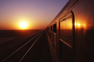 Foto da lateral de um trem em direção ao sol no horizonte