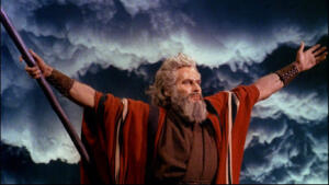 Captura do trailer do filme "Os Dez Mandamentos", mostrando o ator Charlton Heston interpretando Moisés, com olhar distante e compenetrado e os braços abertos e erguidos, segurando um cajado na mão direita, em frente a um céu intimidador de nuvens carregadas e escuras