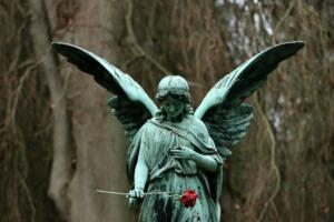 Foto da estátua esverdeada de um anjo segurando uma rosa