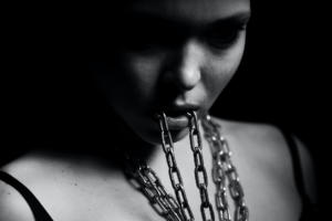 Foto aproximada em tons de cinza de uma mulher segurando uma corrente entre os dentes e em volta do pescoço